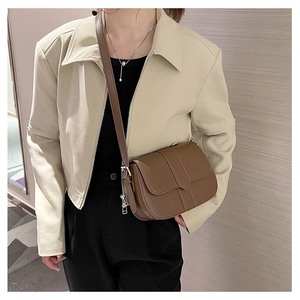 Braune Vintage-Satteltasche mit Zierriemen an Model mit beigefarbener Jacke eines Models
