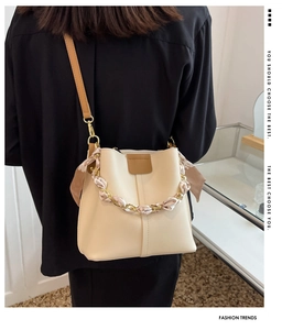 Detail view of beige bucket bag with silk scarf handle and thin brown shoulder strap