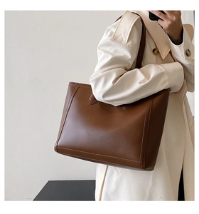 Brown leather tote bag featuring decorative stitching and reinforced handle on a female model