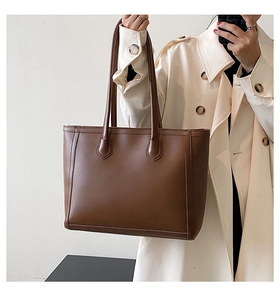 Deep brown large tote bag in synthetic leather shown on a model with an autumn trench coat