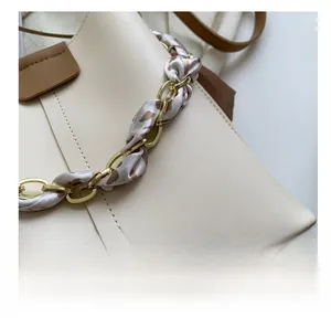 Close-up of beige bucket bag with gold chain handle and leopard print ribbon detail