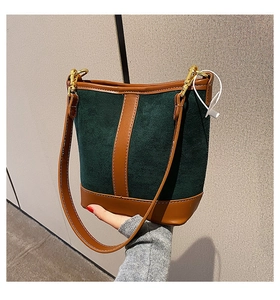 Detail of dark green suede bucket bag with brown leather trim and gold metal hardware