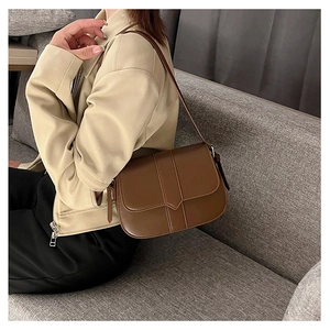Nahaufnahme einer dunkelbraunen Satteltasche aus Leder am beigen Lederjacken-Outfit