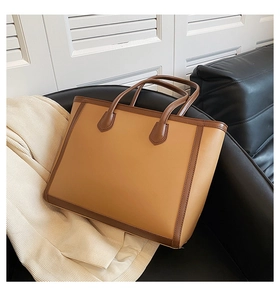 Close-up of dual-tone large tote bag with brown handles on a black leather sofa