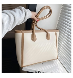 Detail of a large beige tote bag with brown trim held by hand near a window