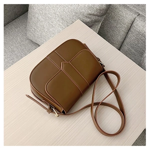 Braune Satteltasche aus Kunstleder mit Kreuzstichdetails und verstellbarem Riemen auf Holz