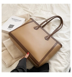 Chic two-tone brown tote bag shown diagonally on a soft white fabric with a book