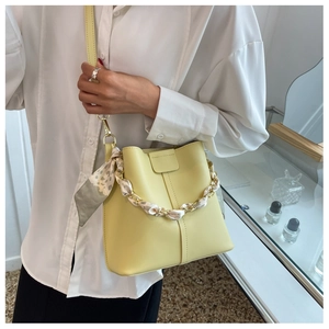 Detail of light yellow bucket bag with a floral scarf wrapped around the chain strap