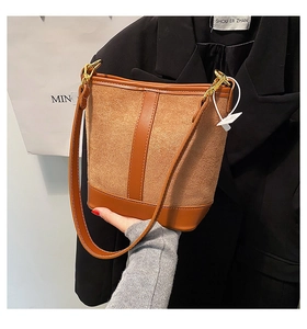 Detail of a brown patchwork bucket bag with suede texture and gold hardware accents