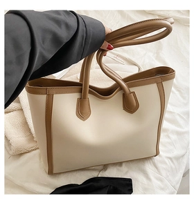 Detail shot of a large tote bag in beige with dark brown trim and dual handles