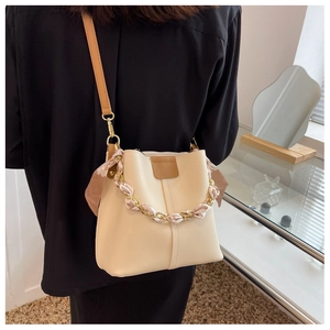 Close-up of cream leather bucket bag with silk-wrapped chain handle and brown strap