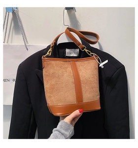 Detailed view of brown bucket bag with mixed textures, gold hardware and leather strap