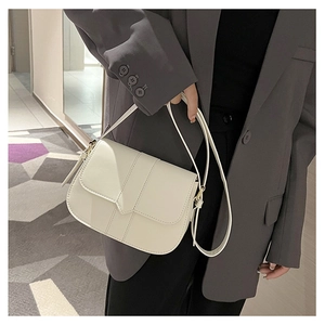 Retro cremeweiße Satteltasche mit Goldbeschlägen über der Schulter auf grauem Blazer