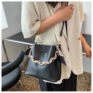 Detail of a black bucket bag with a gold chain handle and leopard print silk scarf