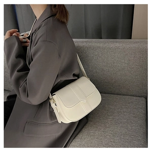 Detail der cremeweißen Satteltasche aus Leder mit goldener Schnalle an grauem Blazer