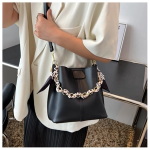 Detail of a black bucket bag with a chain handle wrapped in a beige patterned silk scarf