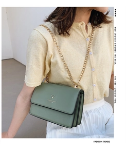 Detail of green leather crossbody bag with deer head emblem and golden chain strap