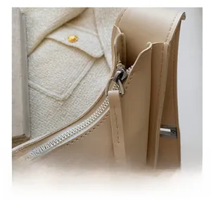 Detail view of smooth silver zipper on a beige textured leather small crossbody bag