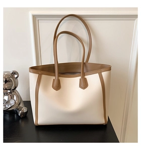Detail view of cream tote bag with brown contrast trim and silver bear ornament