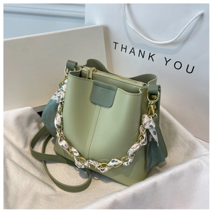 Close-up of light green bucket bag with floral silk scarf handle and golden chain details