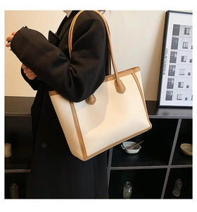 Detail view of large tote bag in beige with brown leather trim shown on shoulder