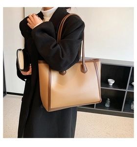 Brown leather tote bag worn by a model in a black wool coat, showing bag scale and fit