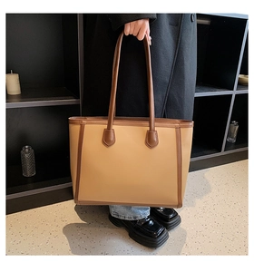 Close-up of minimalist khaki tote bag with dark brown leather handles and stitching