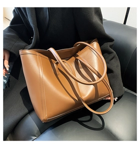 Close-up of caramel brown tote bag with decorative stitching on a dark leather sofa