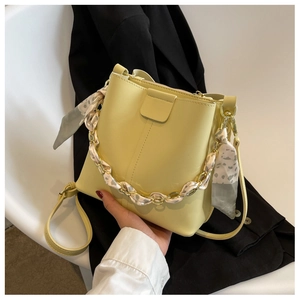 Detail of yellow bucket bag featuring a silk scarf wrapped chain handle and leather finish