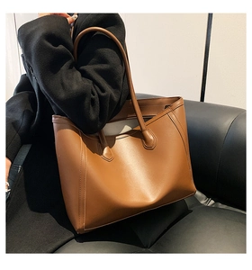 Close-up of a large caramel brown tote bag with stitching detail worn on the shoulder