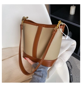 Close-up of beige lychee texture and brown leather stitching on bucket bag with gold hardware