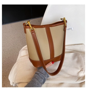 Detail shot of a bicolor bucket bag with beige lychee grain and brown leather trim