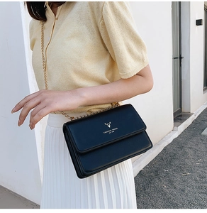 Detail of black leather crossbody bag with golden chain and deer head logo on model