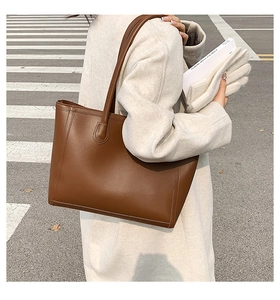 Close-up of textured brown leather tote bag with long handles in an urban street setting