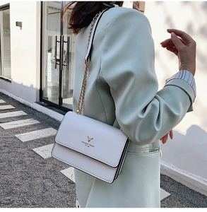 Close-up of minimalist white shoulder bag with gold deer logo and metal chain strap