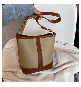 Close-up of beige and brown leather bucket bag showing stitching and golden hardware detail