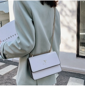 Close-up of a white crossbody bag featuring a golden deer logo and chain strap