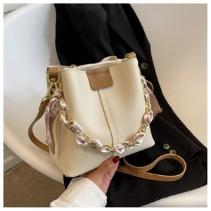 Close-up of cream bucket bag with silk scarf wrapped chain handle and leather trim