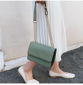Detail of light green leather crossbody bag with gold deer logo and chain strap