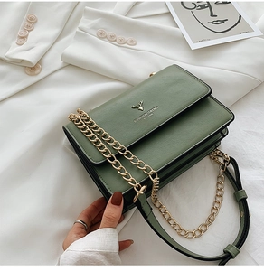 Detail of green leather crossbody bag with golden deer logo on white blazer background