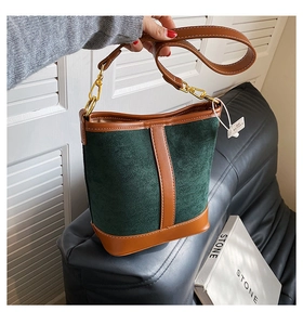 Detailed macro view of dark green suede bucket bag with brown leather trim and gold hardware