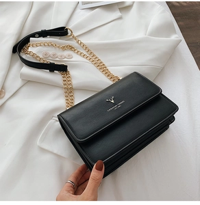 Detail of black textured leather bag with gold deer head buckle and chain strap on white suit
