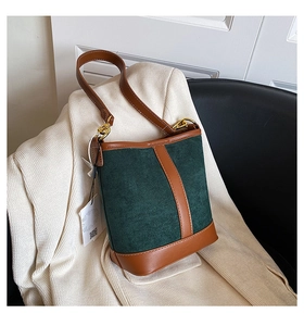 Close-up of dark green suede bucket bag with brown leather trim and golden buckle detail