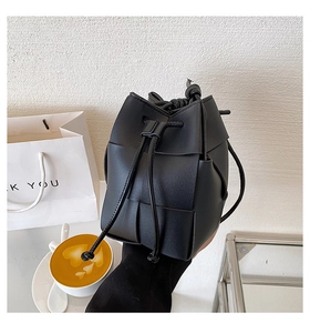 Detail of hand-woven black bucket bag with drawstring closure and fine leather strap