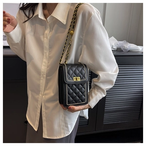 Detail of black quilted crossbody bag with gold rivets and metallic chain strap