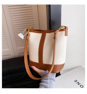 Close-up of litchi grain cream and brown bucket bag with golden hardware detail