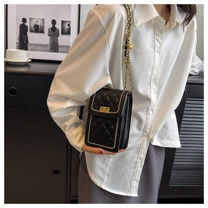 Detail of black quilted chain bag with gold twist lock and bead trim on white shirt