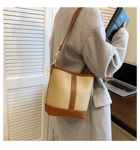Detail of a two-tone bucket bag featuring beige pebble leather and brown smooth trim