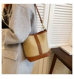 Detail of a beige and brown leather bucket bag featuring pebbled texture and gold hardware