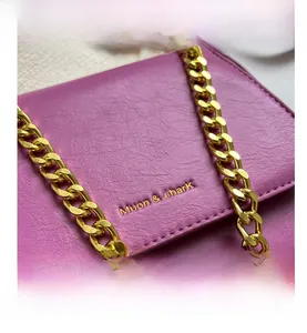 Detail view of purple faux leather crossbody bag with gold logo and chunky chain strap